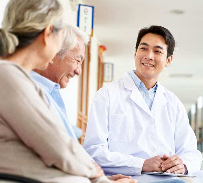 friendly young asian doctor talking to old couple in hospital hallway