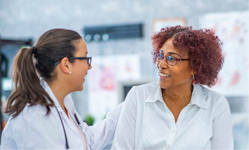 An African American woman smiles lightly as she discusses with the doctor sitting beside her. They are in a medical office.